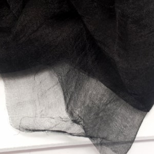 Puede incluir: Primer plano de una tela negra transparente con una textura delicada y fluida. La tela est&aacute; drapeada, creando pliegues y sombras suaves. El material parece ligero y ligeramente transparente, con un brillo sutil.
