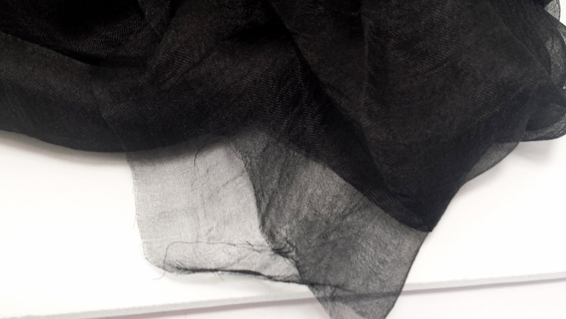 Puede incluir: Primer plano de una tela negra transparente con una textura delicada y fluida. La tela est&aacute; drapeada, creando pliegues y sombras suaves. El material parece ligero y ligeramente transparente, con un brillo sutil.
