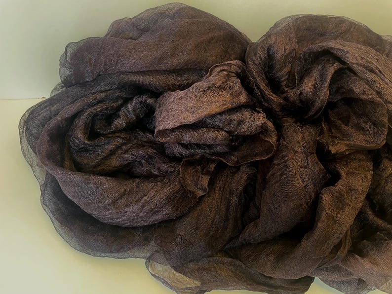 Puede incluir: Una tela transparente de color marr&oacute;n oscuro est&aacute; arrugada, creando una apariencia texturizada y en capas. La tela tiene una textura ligeramente arrugada y parece ligera. El color var&iacute;a de un marr&oacute;n oscuro a un tono m&aacute;s claro, casi p&uacute;rpura en algunas &aacute;reas.
