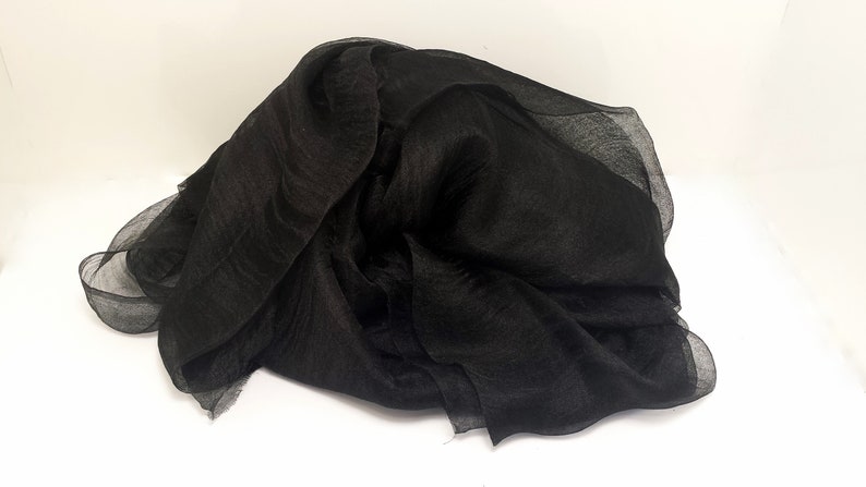Puede incluir: Una bufanda negra drapeada hecha de una tela transparente y fluida. La bufanda est&aacute; arrugada y doblada, creando un efecto de capas. La tela tiene un brillo sutil y los bordes est&aacute;n ligeramente deshilachados.