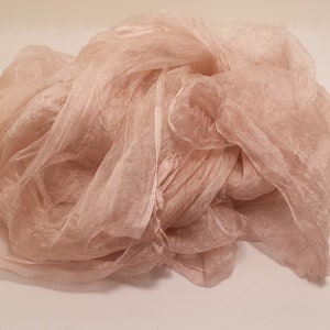 May include: A soft, sheer, blush-colored fabric scarf. The fabric is loosely draped and has a delicate, flowing texture.