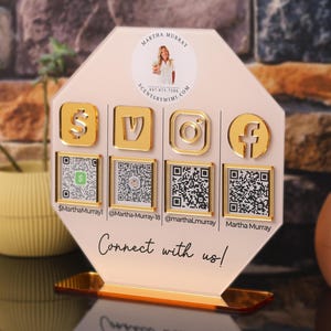May include: An octagonal light pink acrylic social media sign with a gold base. It features a circular photo of a person, four gold social media icons, four QR codes, and the text "Martha Murray," "SCENTBYMIMI.COM," and "Connect with us!" in black.