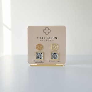 Custom acrylic QR code sign with three QR codes, gold social media icons and personalized business branding, displayed on a reflective countertop
