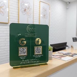 Custom acrylic QR code sign with three QR codes, gold social media icons and personalized business branding, displayed on a reflective countertop