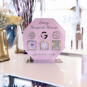 Custom acrylic QR code sign with three QR codes, gold social media icons and personalized business branding, displayed on a reflective countertop