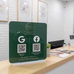 May include: A dark green square acrylic sign for Opulence Salon MN featuring white Google and Facebook logos, two QR codes, and text that reads Leave Us a Review and Wigs By Opulence Salon MN, all mounted on a white rectangular base.