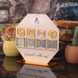 Custom acrylic QR code sign with four QR codes, gold social media icons and personalized business branding, displayed on a reflective countertop