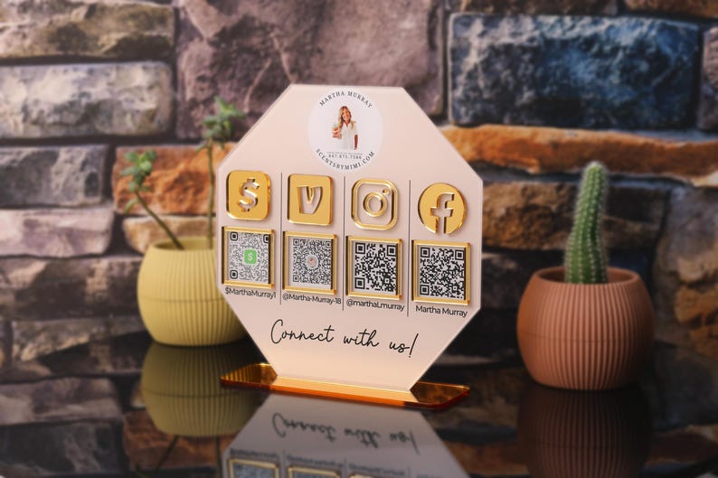 Custom acrylic QR code sign with four QR codes, gold social media icons and personalized business branding, displayed on a reflective countertop