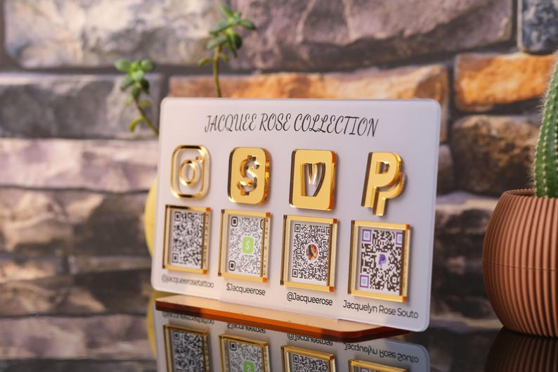 Custom acrylic QR code sign with four QR codes, gold social media icons and personalized business branding, displayed on a reflective countertop