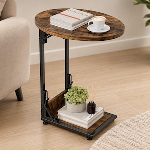 May include: An oval side table with a dark brown wood-grain top and a black metal frame. The table features a C-shaped design with a lower shelf, holding a white coffee cup, books, a small potted green plant, and a dark brown reed diffuser.