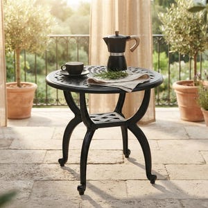 May include: A black metal round side table with a lattice pattern on the tabletop and a lower shelf. The table features four curved legs and is topped with a black moka pot, a small black coffee cup on a saucer, and a folded beige cloth napkin.
