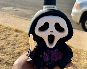 May include: A black and white soap dispenser shaped like a hooded figure with a white mask and a small white knife. The figure has a black hooded robe and a black pump mechanism on top. A pink and black sticker with text is on the front.