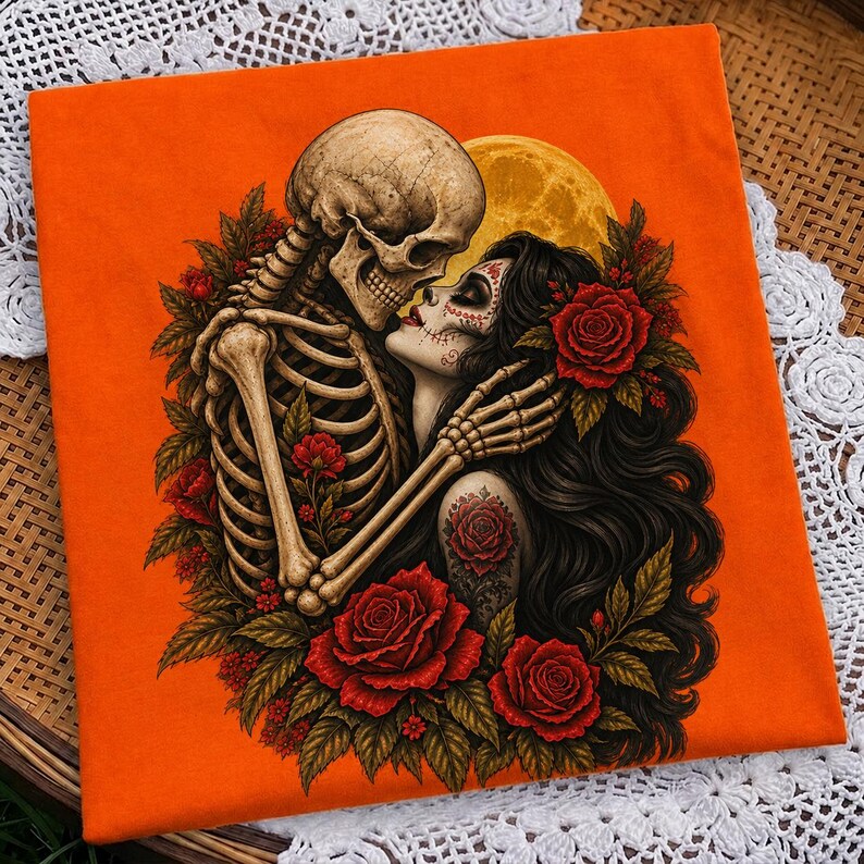 May include: An orange t-shirt featuring a graphic illustration of a skeleton embracing a person with long dark hair and sugar skull makeup. The design includes vibrant red roses, green leaves, and a large yellow moon set against the bright orange fabric.