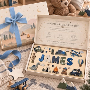 Puede incluir: Un rompecabezas de madera con nombre en una caja de regalo que muestra el nombre JAMES en letras azules y blancas, rodeado de formas de madera que incluyen un dinosaurio, un oso, una fogata, una tienda de campaña, un biplano, un jeep y montañas.