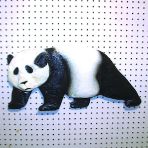 May include: A black and white panda bear figurine with a textured surface. The panda is standing on a white background with small holes.