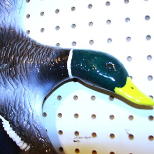 K&ouml;nnte beinhalten: Keramik-Entenskulptur im Flug, mit gl&auml;nzendem Finish. Die Ente hat einen dunkelgr&uuml;nen Kopf mit gelbem Schnabel und wei&szlig;em Halsband. Die Fl&uuml;gel sind eine Mischung aus dunkelblau und hellblau, mit wei&szlig;en Akzenten.