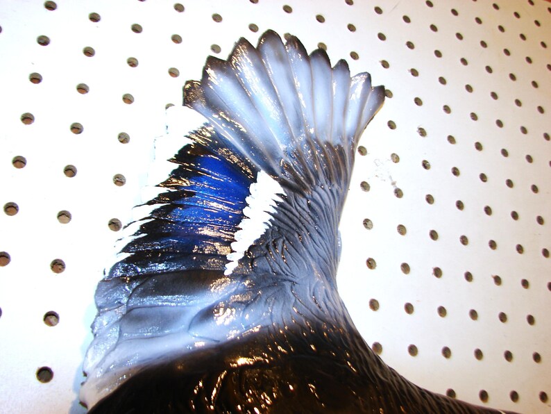 K&ouml;nnte beinhalten: Nahaufnahme eines Vogelfl&uuml;gels mit Farbverlauf. Der Fl&uuml;gel wechselt von tiefem Schwarz zu leuchtendem Blau, mit wei&szlig;en Akzenten an den Kanten. Der Fl&uuml;gel ist gl&auml;nzend und scheint Teil eines dekorativen Objekts zu sein.