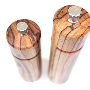 K&ouml;nnte beinhalten: Zwei Salz- und Pfefferstreuer aus Holz mit Holzmaserung. Die Streuer haben silberne Oberteile mit einem 'S' und 'P' darauf.