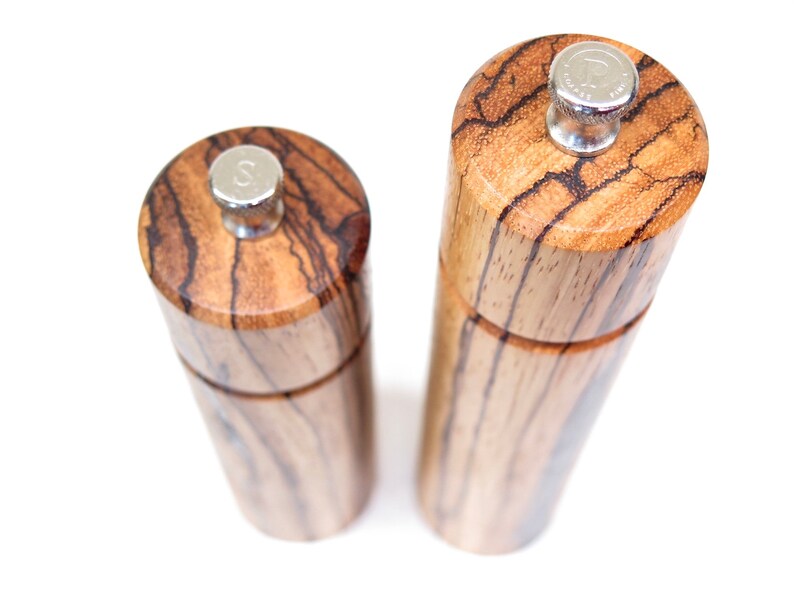 K&ouml;nnte beinhalten: Zwei Salz- und Pfefferstreuer aus Holz mit Holzmaserung. Die Streuer haben silberne Oberteile mit einem 'S' und 'P' darauf.