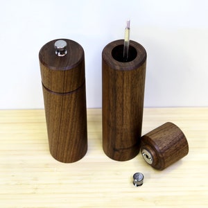 May include: A set of three wooden pepper mills with a dark brown finish. One mill is assembled, another is partially disassembled, and the third is open, revealing the grinding mechanism. The mills have a cylindrical shape with a silver top.