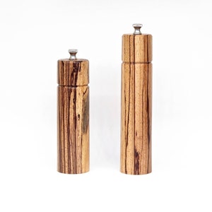 K&ouml;nnte beinhalten: Zwei Salz- und Pfefferstreuer aus Holz mit einem gestreiften Holzmaserungsmuster und silbernen Oberteilen.
