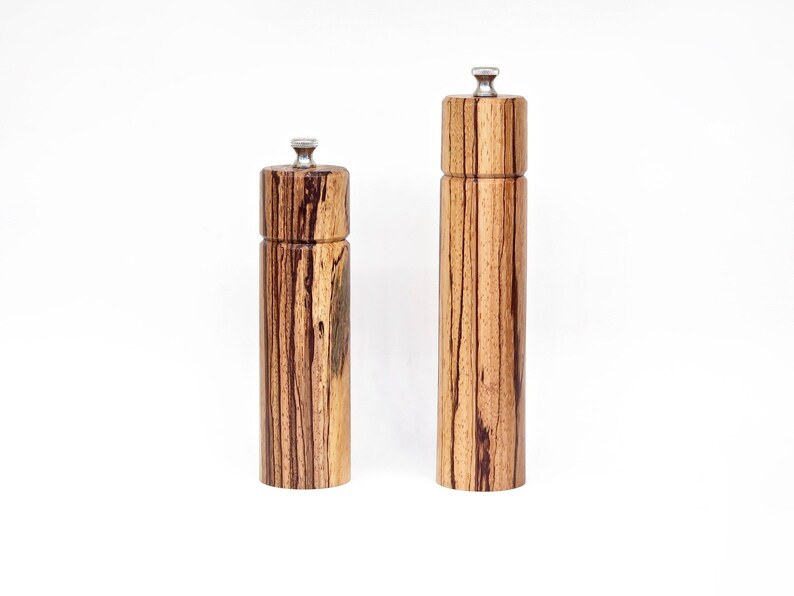 K&ouml;nnte beinhalten: Zwei Salz- und Pfefferstreuer aus Holz mit einem gestreiften Holzmaserungsmuster und silbernen Oberteilen.