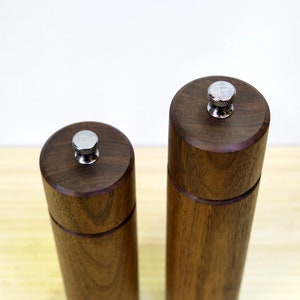 May include: Two wooden salt and pepper grinders. The grinders are made of dark brown wood with a cylindrical shape. Each grinder has a silver-colored top with a letter on it, one with an "S" and the other with a "P".