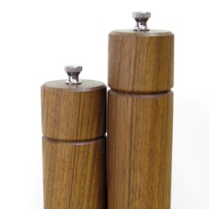 May include: Two wooden salt and pepper grinders with a natural wood grain finish. The grinders have a cylindrical shape with a silver-colored top. The taller grinder is approximately 8 inches tall, and the shorter one is about 6 inches tall.
