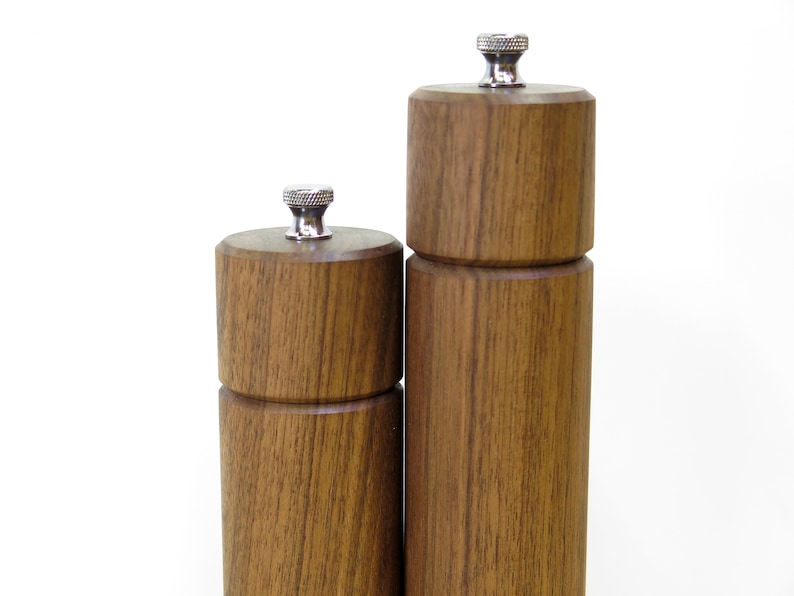 May include: Two wooden salt and pepper grinders with a natural wood grain finish. The grinders have a cylindrical shape with a silver-colored top. The taller grinder is approximately 8 inches tall, and the shorter one is about 6 inches tall.
