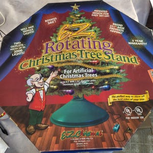 May include: A product box for an E.Z. Rotating Christmas Tree Stand. The box features a graphic of a decorated tree, a cartoon character, and text including 'Rotates 360!', 'Broad 23.5 inch base', and 'For artificial trees up to 8.5 feet'.