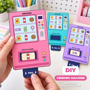 May include: A pink, blue, and purple paper DIY vending machine craft set. Each rectangular card features a grid of snack illustrations, a keypad, and a pull-out tab labeled PULL at the bottom. The text SNACKS and PICK UP HERE is printed on each.