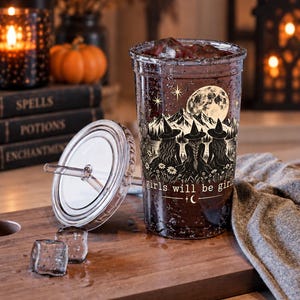 May include: A clear plastic tumbler with a lid and straw, featuring a graphic of three witches in hats standing before mountains and a full moon. The text "girls will be girls" is printed below the illustration, accompanied by small star and moon icons.