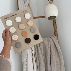 Peut inclure: Un panneau d'échantillons beige rectangulaire intitulé GLAZE SAMPLES par MUDDY HEART présentant douze disques en céramique circulaires avec diverses finitions et couleurs, dont Gloss White, Matte White, Frost White, Sand, Textured White, Clay, Matte Grey, Unearthed, Buff, Espresso et Frost Black.