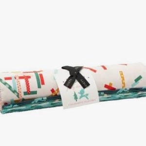 May include: A rolled bundle of fabric strips featuring a cream background with a pattern of small red, green, and yellow rectangular shapes. A black ribbon ties the roll, holding a white tag with a small green deer and tree graphic.
