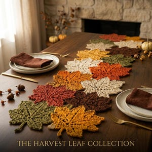 May include: A crochet table runner composed of interconnected maple leaf motifs in shades of orange, brown, cream, and olive green. The runner is arranged on a wooden table with plates, napkins, and small decorative pumpkins and acorns.