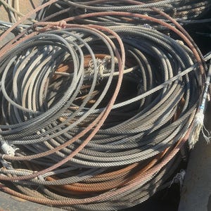 May include: A collection of coiled ropes featuring a mix of grey and brown tones. The ropes are constructed from twisted fibres and are layered in a circular pattern, showing frayed ends and metallic-coloured accents at the tips of the strands.