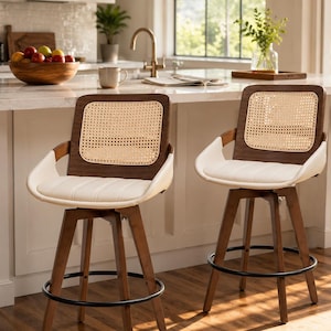 May include: Two swivel bar stools featuring dark brown wooden frames, cream-colored upholstered seats, and backrests with woven cane inserts. Each stool has four legs connected by a circular black metal footrest ring for stability and support.