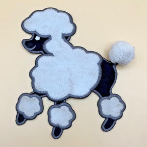 May include: A black and white poodle dog patch featuring a fuzzy white head, chest, and leg puffs, with a black body and a distinct white pom-pom tail. The embroidered design is outlined in a dark grey border, creating a clear silhouette of the animal.