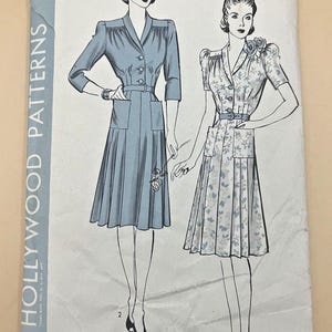 Könnte beinhalten: Ein Vintage-Schnittmusterumschlag von Hollywood Patterns, Nummer 676, Größe 20, 38 Oberweite, 41 Hüfte. Die Abbildung zeigt zwei Kleider-Varianten: ein einfarbig blaues mit Dreiviertelärmeln und ein geblümtes mit kurzen Ärmeln, beide mit Gürteln und Taschen.