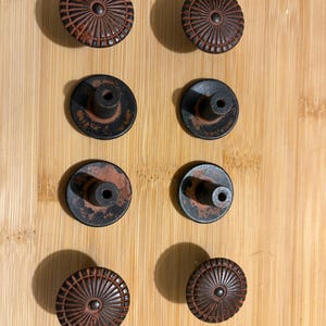 May include: A set of four round cabinet knobs with a dark brown finish and a radial, sunburst-like pattern on the front. Each knob features a central circular protrusion and a cylindrical mounting post on the back with a central screw hole.