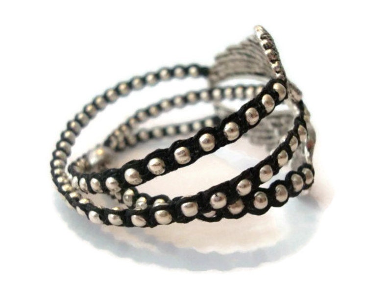 K&ouml;nnte beinhalten: Ein schwarzes und silbernes Perlenarmband mit einem dekorativen Metalldesign. Das Armband besteht aus mehreren Str&auml;ngen schwarzer Schnur mit silbernen Perlen.