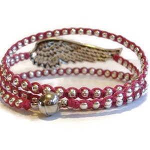 May include: A red wrap bracelet with silver beads and a silver wing charm. The bracelet has a magnetic clasp.