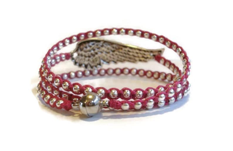 May include: A red wrap bracelet with silver beads and a silver wing charm. The bracelet has a magnetic clasp.