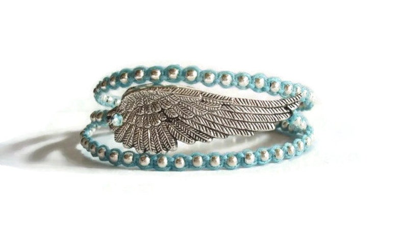 Puede incluir: Un brazalete de envoltura de cuentas azul turquesa con un dije de ala de &aacute;ngel plateado.
