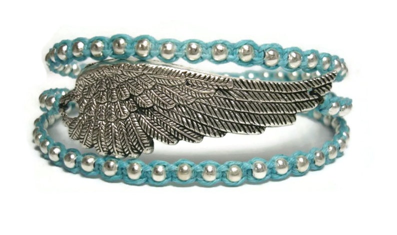 Puede incluir: Un brazalete de envoltura de cuentas turquesa con un dije de ala de plata. El brazalete est&aacute; hecho de m&uacute;ltiples hebras de cord&oacute;n turquesa con cuentas de plata.