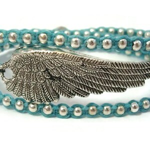 Puede incluir: Un brazalete de envoltura azul turquesa con cuentas plateadas y un dije de ala plateada.