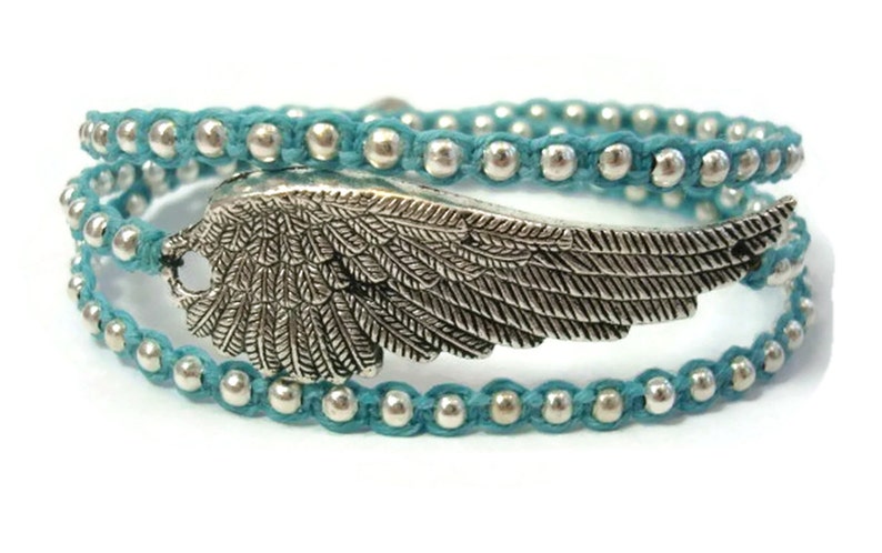 Puede incluir: Un brazalete de envoltura azul turquesa con cuentas plateadas y un dije de ala plateada.