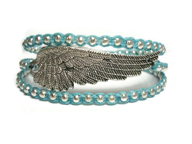 Puede incluir: Un brazalete de envoltura azul turquesa con cuentas plateadas y un dije de ala plateada.