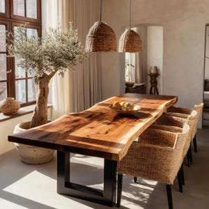 Peut inclure: Une table de salle à manger en bois à bord brut avec une finition grain naturel et des pieds en métal noir en forme de U. La table est entourée de quatre fauteuils en rotin tressé et deux suspensions assorties en osier.