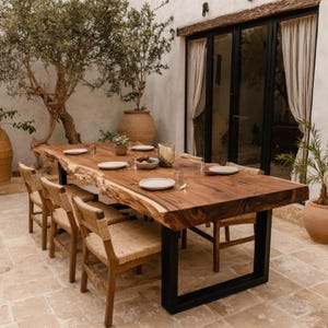 Puede incluir: Una mesa de comedor rectangular grande con una superficie de madera natural de borde vivo y patas de metal negro en forma de U. La mesa está puesta con platos blancos, vasos transparentes y un cuenco, rodeada de sillas de madera con asientos tejidos.